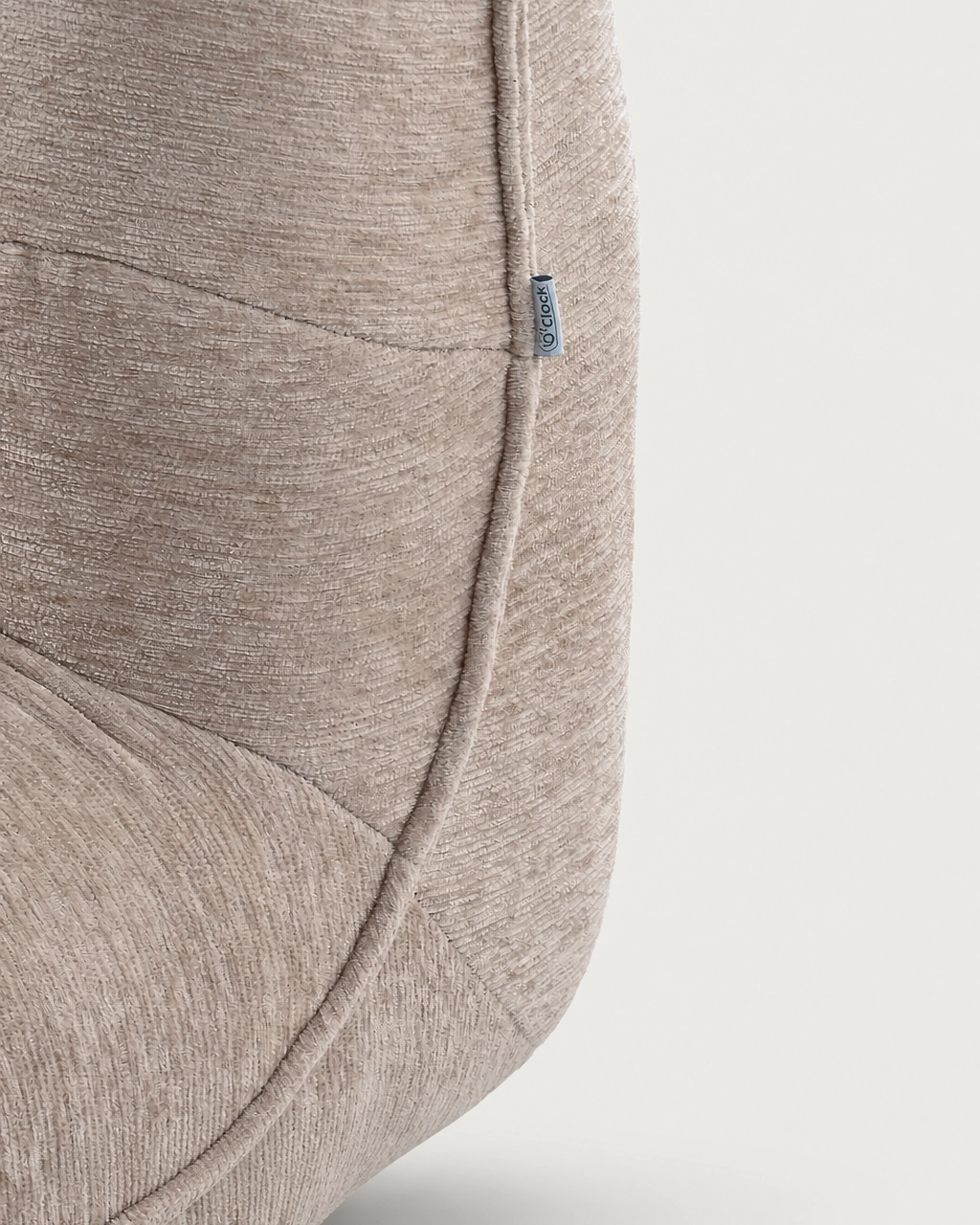Zeca Upholstered Armchair in sand beige textured fabric, close-up of piped seams and side tag
